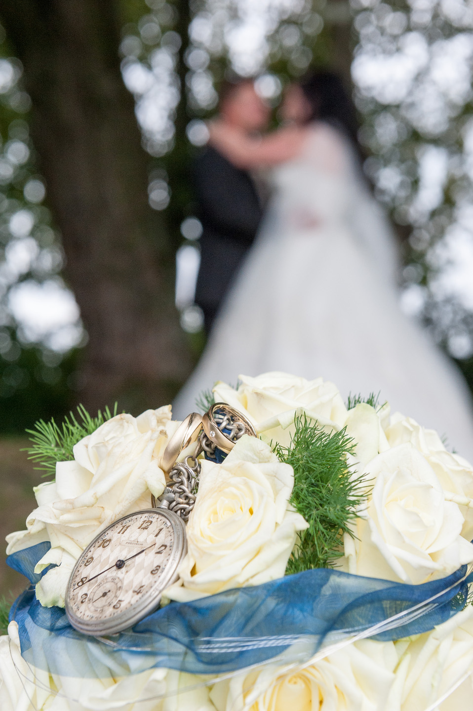 Wunderschönes Hochzeitsfoto mit Brautstrauß im Vordergrund und unscharfem Brautpaar im Hintergrund.